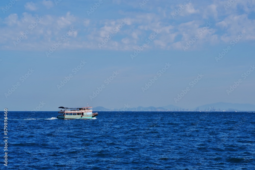 Passenger boat crossing to the island against the blue sea ocean against bright sky.