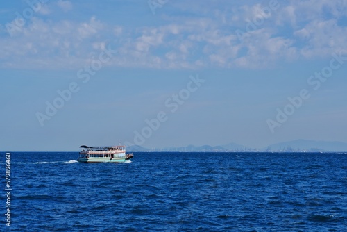 Passenger boat crossing to the island against the blue sea ocean against bright sky. © Kun