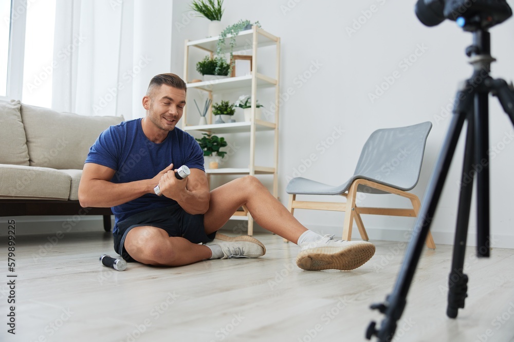 Obraz premium Man athlete blogger records body workout training with dumbbells at home on camera, sports blogger bodybuilder, health and beauty