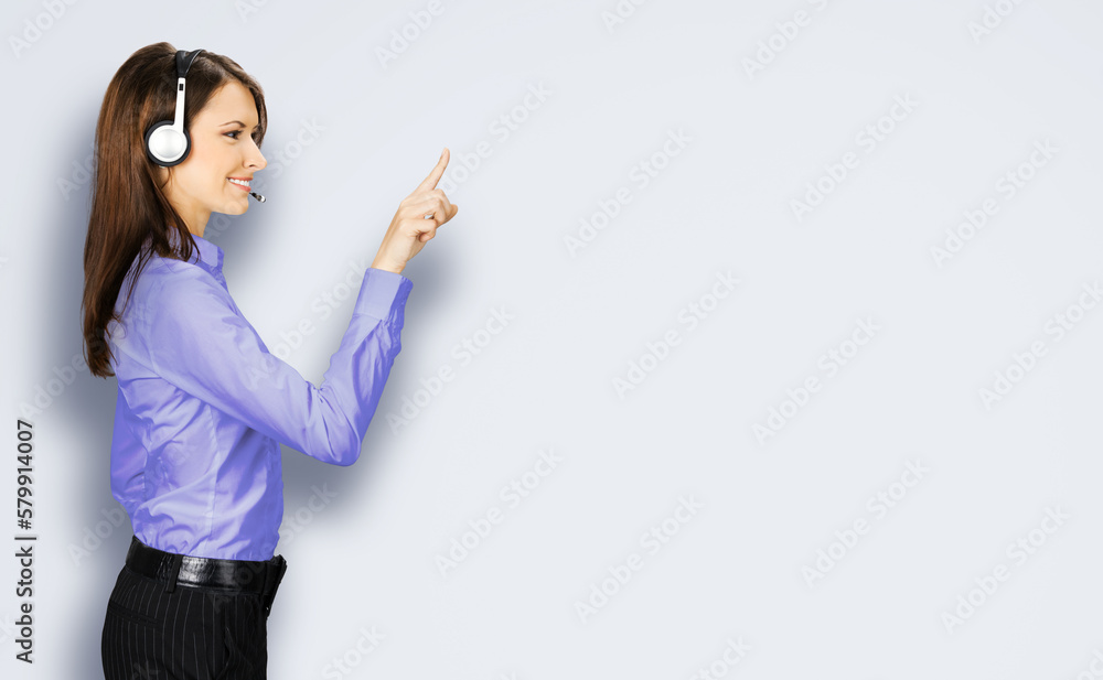 Call center service. Profile side image of customer support phone sales operator in blue cloth, headset show pointing clicking at copy space, imaginary or text, standing on grey gray background Call center service. Profile side image of customer support phone sales operator in blue cloth, headset show pointing clicking at copy space, imaginary or text, standing on grey gray background