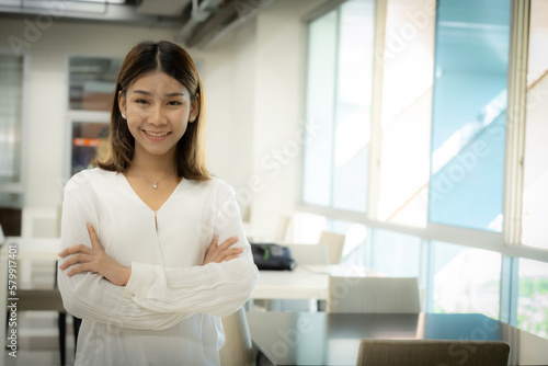 The beautiful asian female teacher is standing with arms crossed and looking at the camera with a smiling face in the classroom.