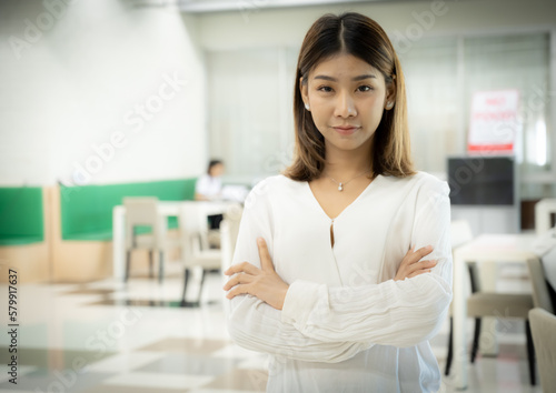 The beautiful asian female teacher is standing with arms crossed and looking at the camera with a serious face in the classroom.