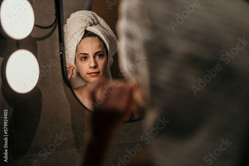 Shot of a young woman cleaning her ear with a cotton bud during her before bed routine.
