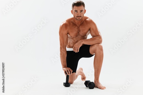 Man athletic body bodybuilder posing with dumbbells with naked torso abs full-length in the background, fitness class. Advertising, sports, active lifestyle, competition, challenge concept. 