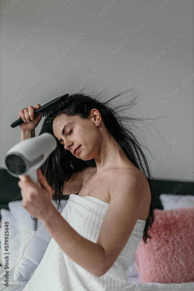Obraz premium Shot of a young woman drying her hair in the bedroom.