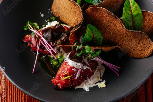 Fototapeta Naklejka Na Ścianę i Meble -  beef tartare with sauce and herbs in a black plate