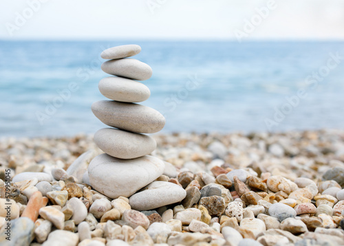A balance of pebble stones is built on a stone beach against the backdrop of the blue sea.