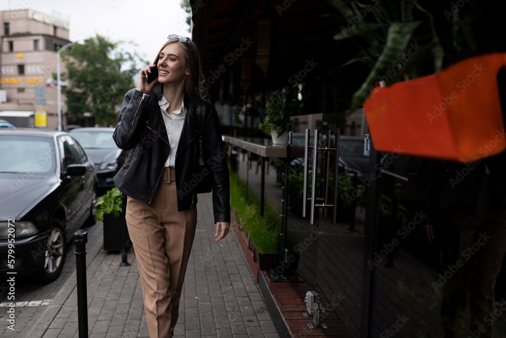 Fototapeta premium successful young adult female student walking around the city and talking on the phone
