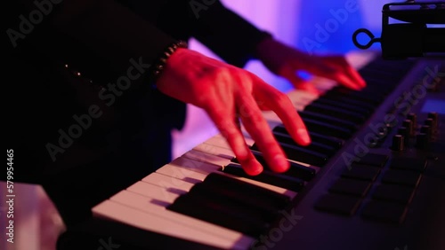 Male hands playing on synthesizer piano. Band at concert stage playing music.