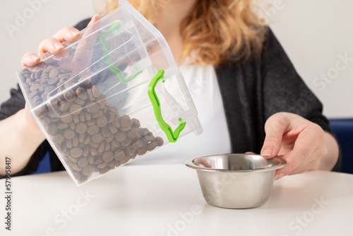 dosage of pet food, the owner measures out a portion of feed for the dog, pours cat food into a bowl from the container photo