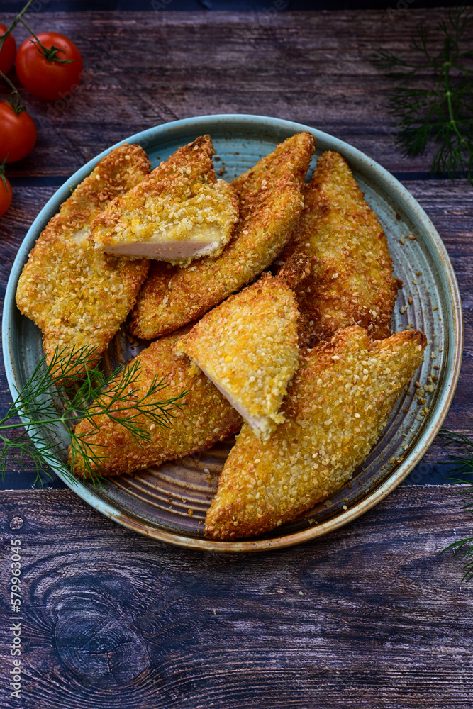
 Crispy oven baked  chicken breast with sesame seeds and ketchup. Breaded chicken fillets  with chilly peppers and fresh basi on wooden rustic background