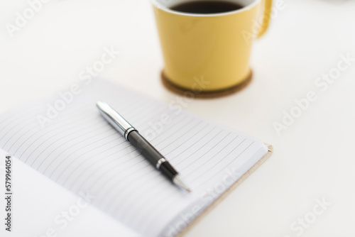 Close-up of book and pen by coffee cup on white background