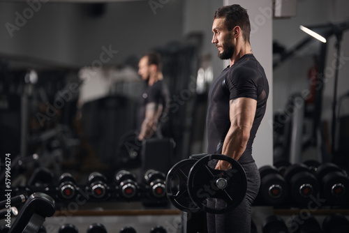 Side view of man lifting barbell while exercising at gym