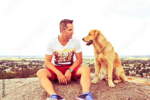 Full length of mid adult man looking at dog while sitting on rock against clear sky photo