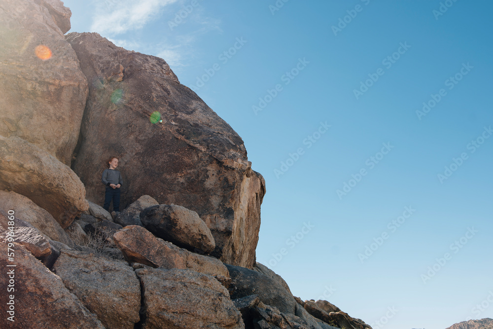 Low angle view of boy standing on rocks against sky during summer Low angle view of boy standing on rocks against sky during summer