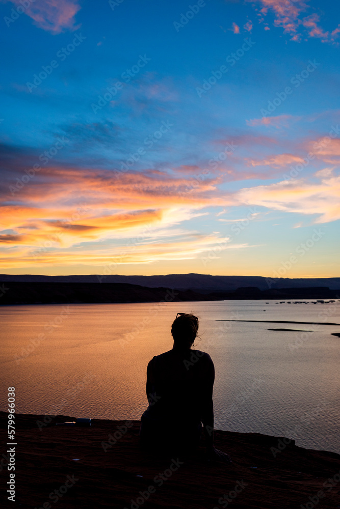 Silhouette woman sitting by river against dramatic sky during sunset Silhouette woman sitting by river against dramatic sky during sunset