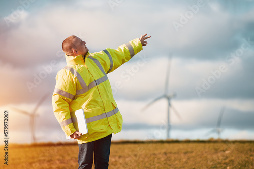 Back view of young male engineer in a wind turbine farm in the background.