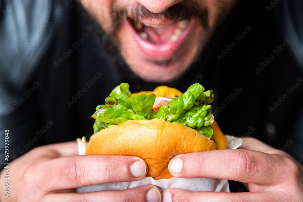 man eating a hamburger with fresh salad, closeup of hands man eating a hamburger with fresh salad, closeup of hands