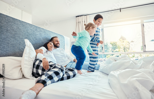 Family, morning and kids jumping on a bed, playing while having fun in the bedroom of their parents. Happy, children or wake up with a brother and sister in a house feeling playful or excited