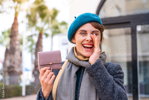 Brunette woman holding a wallet at outdoors shouting with mouth wide open © luismolinero