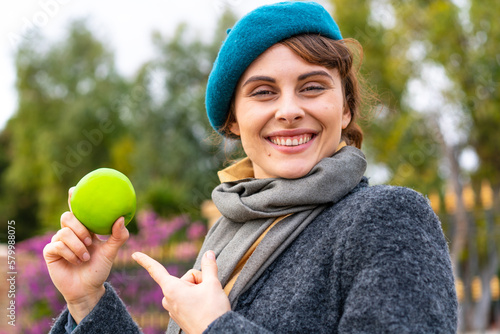 Brunette woman with an apple at outdoors and pointing it
