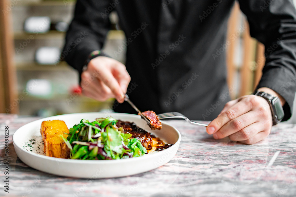 man hands with fork and knife eating beef steak and salad in cafe