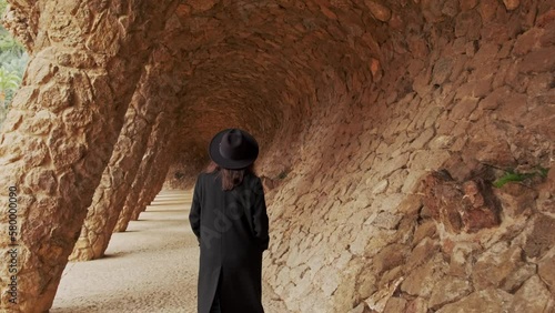 Motion footage of young woman in black hat and coat walking in Guel Park in Barcelona.