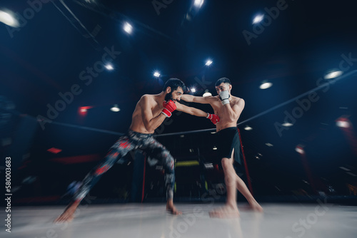 Fototapeta Naklejka Na Ścianę i Meble -  Two man MMA boxers fighters in fights without rules in ring octagon, dark background, motion blur