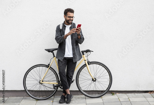 Young handsome man with bicycle over white wall background in a city, cheerful student men with mobile phone smiling outdoor, Modern healthy lifestyle, travel, casual business, connection concept
