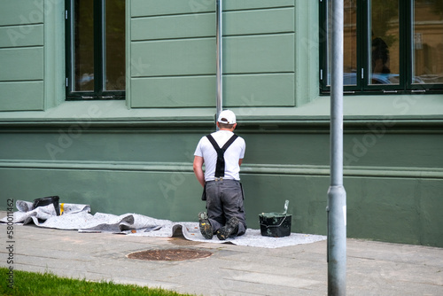 Maler und Lackierer arbeitet mit Pinsel und Farbe an einer Fassade und Regenrinne eines Hauses an einem Bürgersteig, viel Textfreiraum © redaktion93
