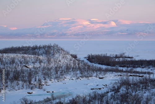 Beautiful sunrise at Abisko Ostra viewpoint. Snowy scenery of mountains and buildings in valley. Abisko National Park (Abisko nationalpark), Sweden, Arctic Circle, Swedish Lapland