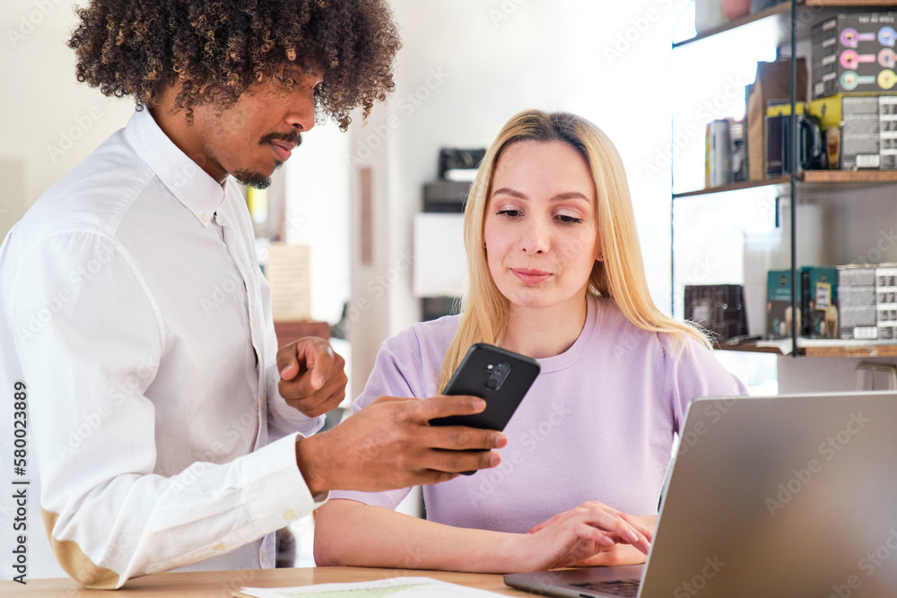 African American guy working together with a blonde Caucasian girl with her smartphone in hand African American guy working together with a blonde Caucasian girl with her smartphone in hand