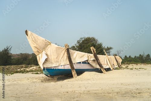 Old boat covered with an awning stands on the sandy shore of the beach