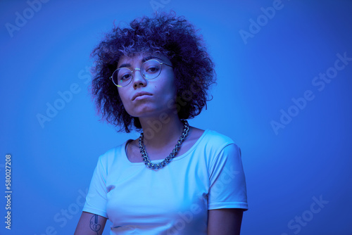 Close-up face portrait of cool kazakh model girl with curls and chain in neon light isolated on studio background