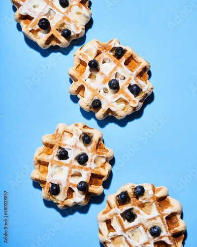 Waffles in blue background with blueberries, honey and nuts.