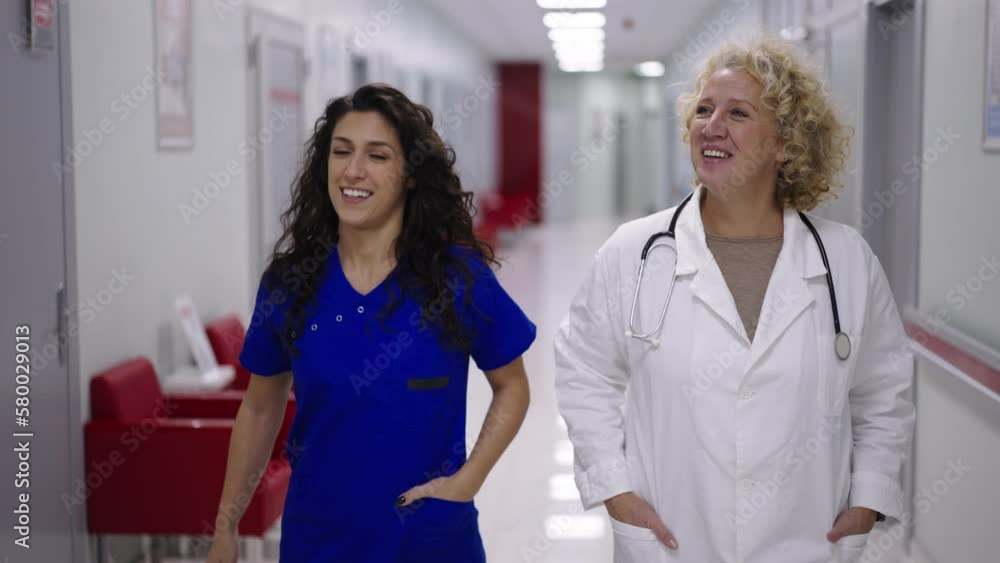 Doctor with lab coat and stethoscope walking with a nurse together and talking in slow-motion through hospital corridor Doctor with lab coat and stethoscope walking with a nurse together and talking in slow-motion through hospital corridor