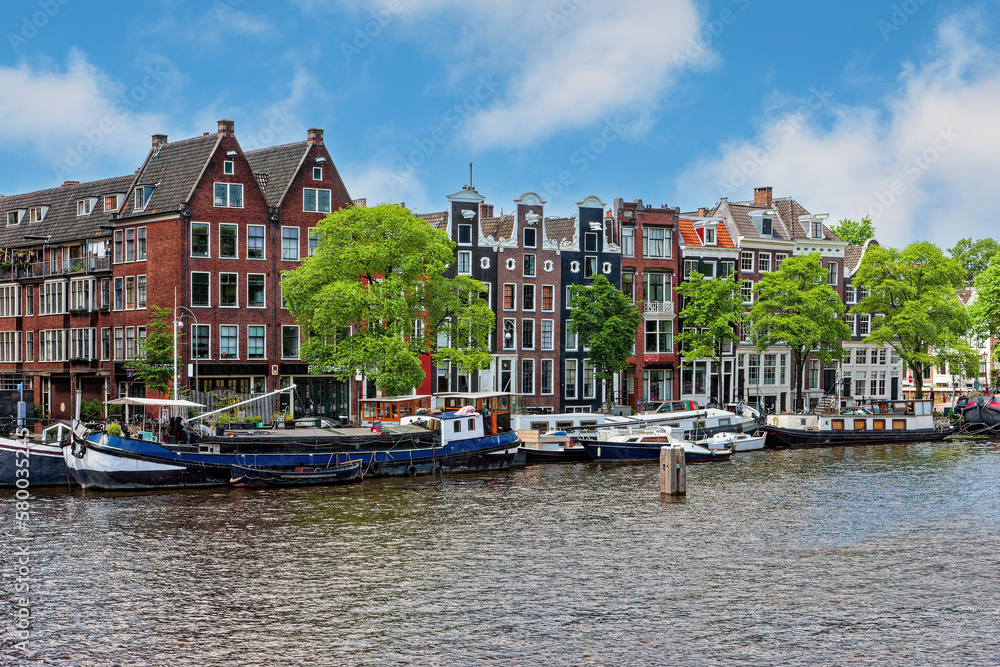 Typical houses with colorful facades in Amsterdam and cruise boats. The Amstel River.
