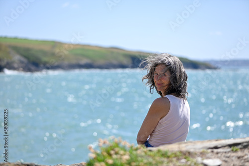 Portrait d'une femme cinquantenaire, cheveux aux vents, mer en arrière-plan 