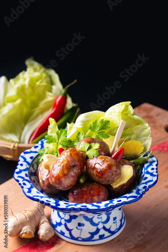 Food concept Sai krok Isan or Isaan Thai-Laos fermented pork and rice sausages in Tradition thai ceramic pedestal plate on black background with copy space