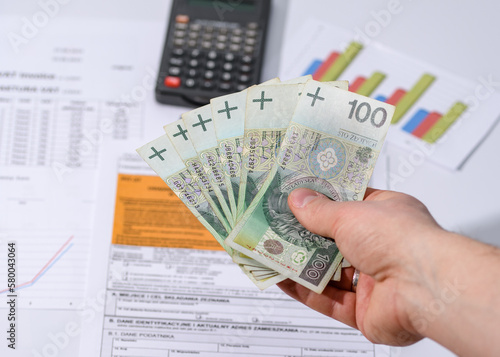 Banknoty 100 złotych trzymane w ręce na tle papierów i kalkulatora pln