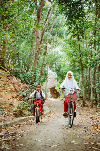 boy and girl in elementary school uniform cycling happily at country road