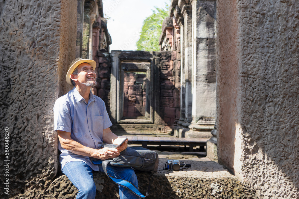 asian senior man traveller smiling and sitting on walkway the door of old architecture in Phimai historical park,Thailand, concept elderly people interested in historical tourism asian senior man traveller smiling and sitting on walkway the door of old architecture in Phimai historical park,Thailand, concept elderly people interested in historical tourism
