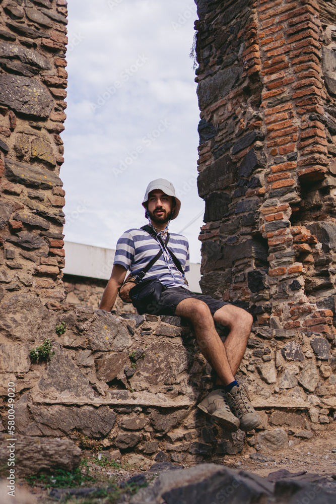 Low angle view of a young latin man with a bucket hat sitting in an antique window frame. Vertical photo.