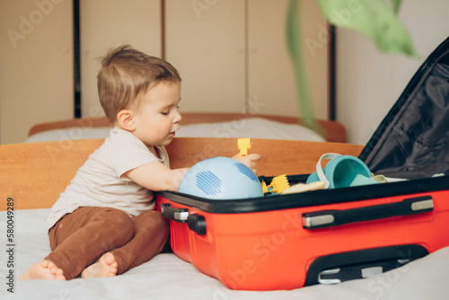 Baby boy and Travel Suitcase. Kid and Luggage Packed for Vacation Full of Clothes, Child and Family Trip.