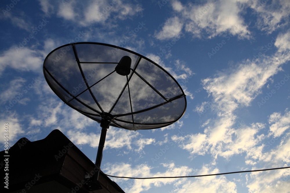 Big Black Satellite Dish on cloudy blue sky.