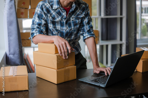 Small business entrepreneur, SME, freelance male working with boxes at home. Use a laptop for commercial auditing. online marketing Packaging Box SME Seller Concept Ecommerce Team online sales © Witoon