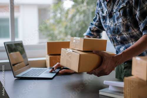 Small business entrepreneur, SME, freelance male working with boxes at home. Use a laptop for commercial auditing. online marketing Packaging Box SME Seller Concept Ecommerce Team online sales © Witoon