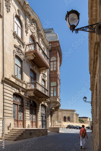 Old town narrow street between carved stone buildings with walking female tourist, Baku Azerbaijan