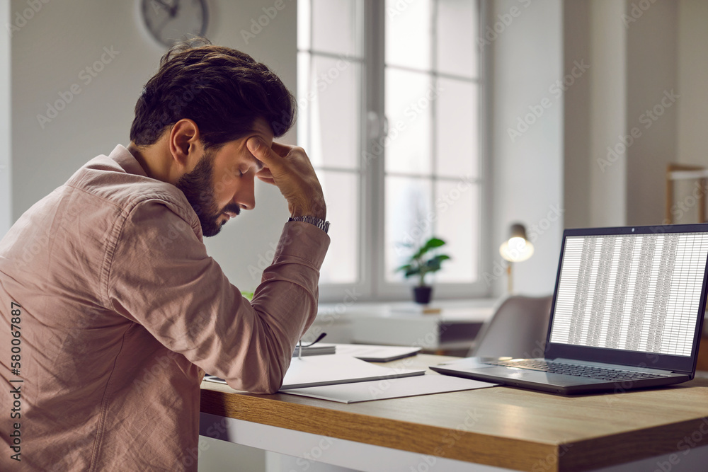 Tired, stressed business man sitting at his working desk with a laptop computer in the office, suffering from a headache and holding his hand on his head. Concept of stress, overworking and burnout Tired, stressed business man sitting at his working desk with a laptop computer in the office, suffering from a headache and holding his hand on his head. Concept of stress, overworking and burnout