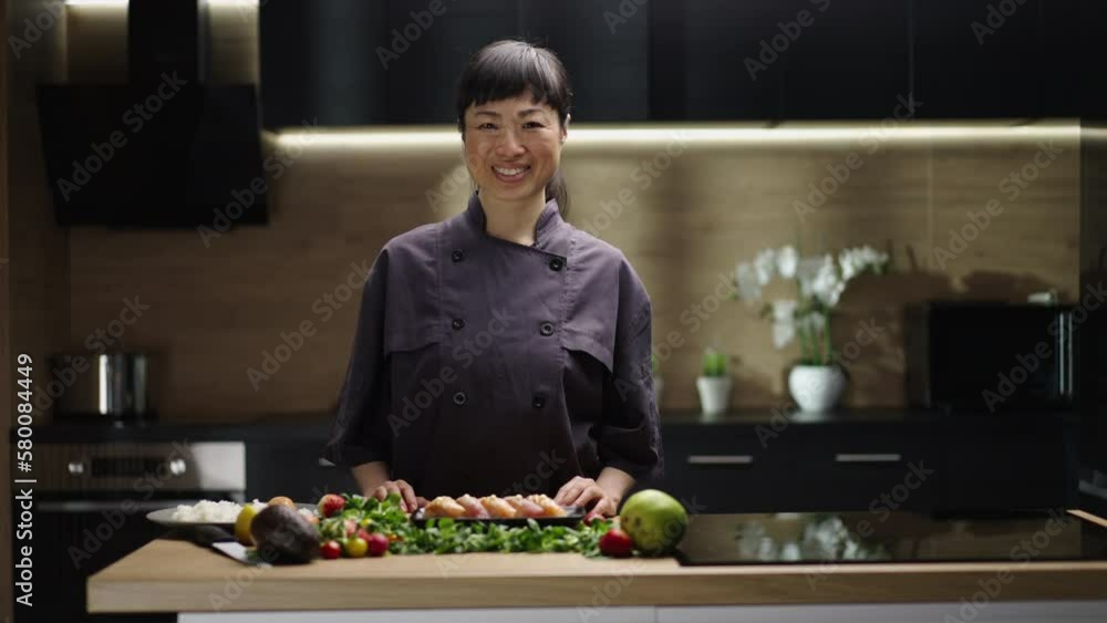 Japanese female chef standing in the kitchen, looking at camera with a tray of sushi and other ingredients Japanese female chef standing in the kitchen, looking at camera with a tray of sushi and other ingredients